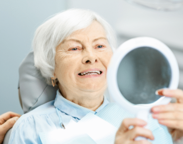 Female patient receiving dental implant treatment at North Down Dental in Bangor, Northern Ireland, smiling in mirror while checking her new teeth.